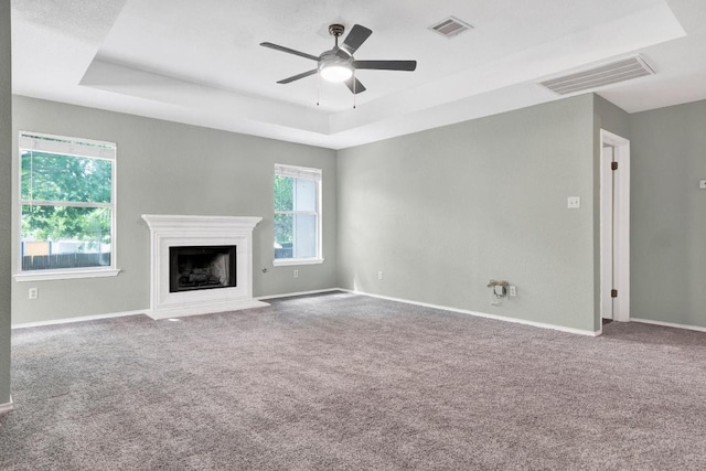 1415 Quicksilver Cir, Round Rock, TX 78665 - unfurnished living room featuring a tray ceiling, carpet flooring, a ceiling fan, and a fireplace with flush hearth