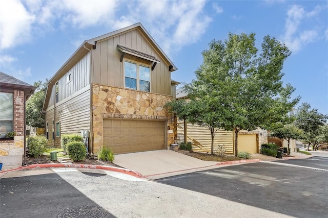 view of front of house featuring stone siding, an attached garage, driveway, and board and batten siding