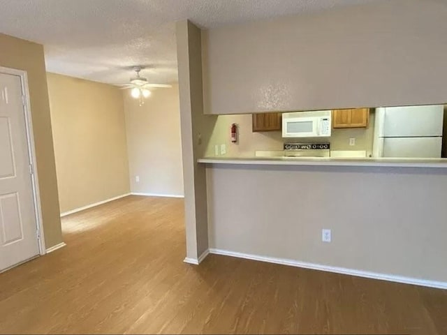 1202 Thorpe Ln Unit 211, San Marcos, TX 78666 - kitchen featuring ceiling fan, a textured ceiling, wood finished floors, baseboards, and white appliances