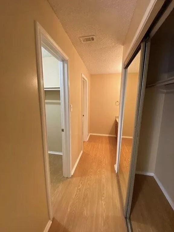1202 Thorpe Ln Unit 211, San Marcos, TX 78666 - hallway featuring a textured ceiling, visible vents, baseboards, and light wood finished floors