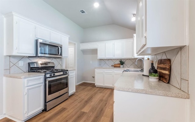 208 Bastian Ln, Georgetown, TX 78626 - kitchen with stainless steel appliances, a sink, light wood-style flooring, vaulted ceiling, and tasteful backsplash