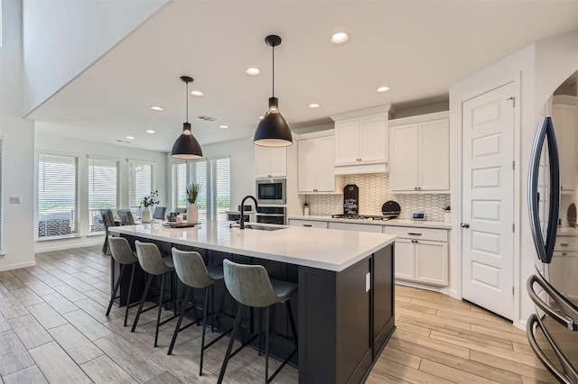 1205 Bluewood Bnd, Leander, TX 78641 - kitchen with a sink, light wood-style flooring, a center island with sink, stainless steel appliances, and decorative backsplash