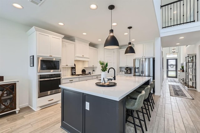 1205 Bluewood Bnd, Leander, TX 78641 - kitchen featuring stainless steel appliances, light wood-style flooring, decorative backsplash, white cabinets, and a spacious island