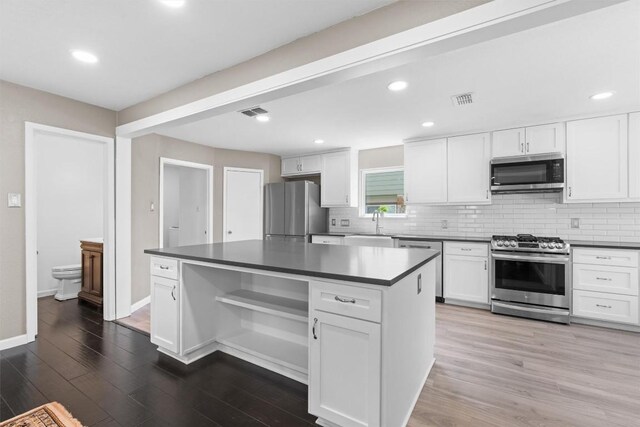 kitchen with stainless steel appliances, dark countertops, backsplash, white cabinets, and recessed lighting