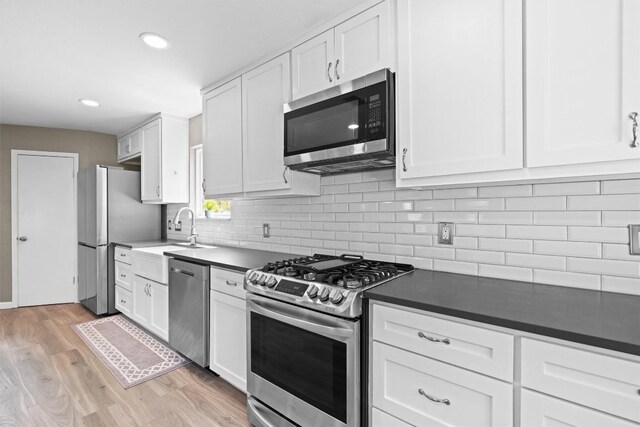 kitchen with stainless steel appliances, a sink, white cabinetry, dark countertops, and recessed lighting