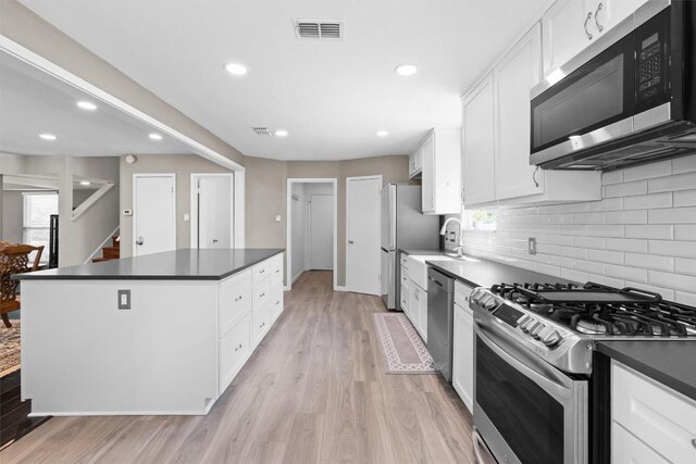 kitchen with appliances with stainless steel finishes, a center island, dark countertops, white cabinets, and recessed lighting