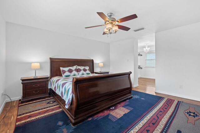 bedroom featuring baseboards, wood finished floors, a ceiling fan, and a chandelier
