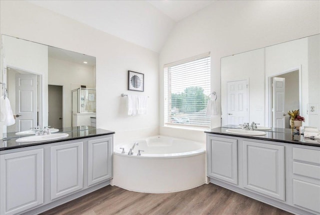 bathroom featuring a bath, wood finished floors, lofted ceiling, and a sink