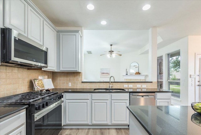 kitchen featuring light wood finished floors, stainless steel appliances, a ceiling fan, a sink, and decorative backsplash