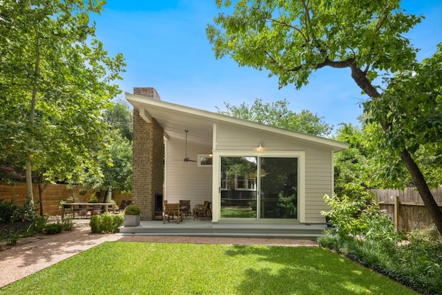 rear view of property featuring a chimney, fence, ceiling fan, a patio, and a lawn