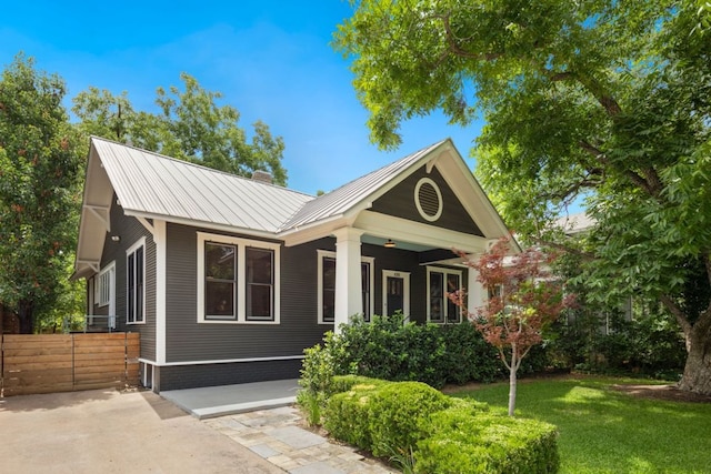 bungalow-style home with metal roof, a front yard, and fence