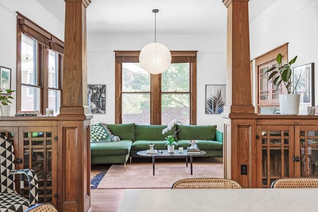 living area featuring a wealth of natural light, wood finished floors, and ornate columns