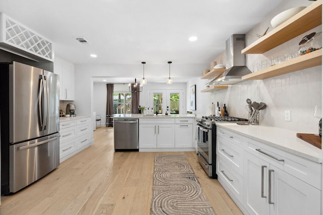 kitchen with stainless steel appliances, wall chimney exhaust hood, a sink, light wood finished floors, and open shelves