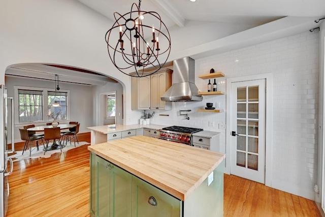 kitchen featuring arched walkways, green cabinets, butcher block countertops, and wall chimney exhaust hood