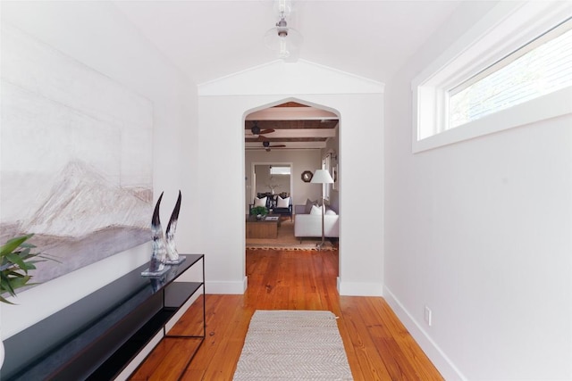hall with arched walkways, light wood-type flooring, baseboards, and beam ceiling