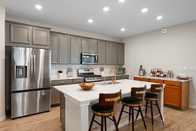 1921 Winston Way, Leander, TX 78641 - kitchen featuring appliances with stainless steel finishes, light wood finished floors, decorative backsplash, a center island with sink, and light countertops
