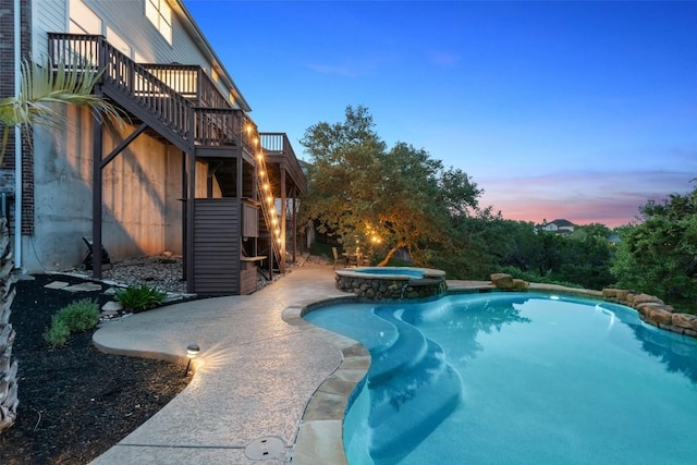 pool at dusk featuring a deck and a pool with connected hot tub