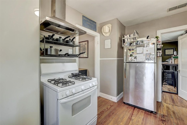 809 E 44th St, Austin, TX 78751 - kitchen featuring freestanding refrigerator, white gas range, wall chimney exhaust hood, wood finished floors, and baseboards