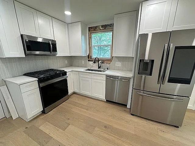 kitchen featuring a sink, stainless steel appliances, light countertops, backsplash, and white cabinetry