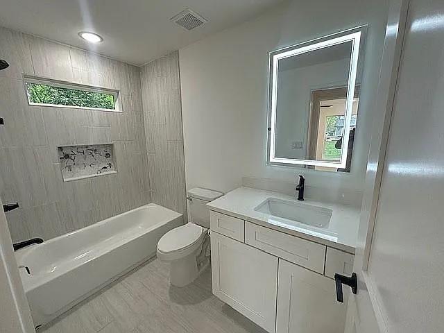 bathroom featuring visible vents, toilet, vanity, and  shower combination