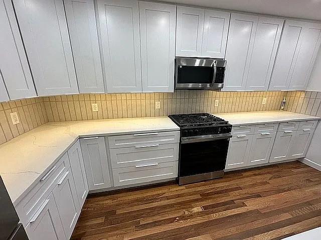 kitchen featuring dark wood finished floors, stainless steel microwave, light stone countertops, black gas stove, and tasteful backsplash