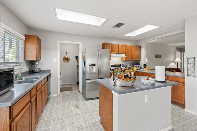 kitchen featuring visible vents, under cabinet range hood, brown cabinets, a sink, and appliances with stainless steel finishes