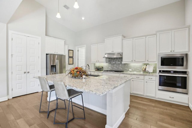 kitchen featuring wood finished floors, under cabinet range hood, appliances with stainless steel finishes, a sink, and high vaulted ceiling