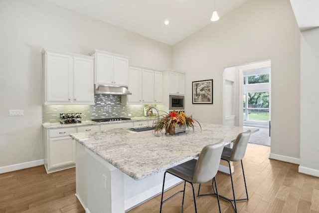 kitchen featuring stainless steel microwave, light wood-type flooring, high vaulted ceiling, and a sink