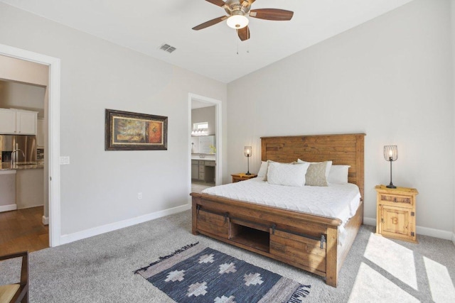 bedroom with baseboards, stainless steel refrigerator with ice dispenser, light carpet, and ensuite bath