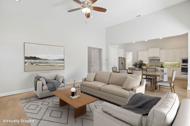 living room featuring light wood-type flooring, recessed lighting, ceiling fan, and a high ceiling