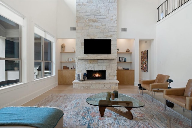 living room featuring baseboards, visible vents, a stone fireplace, and a towering ceiling