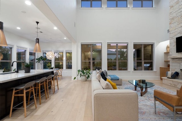 living room featuring a fireplace, a notable chandelier, light wood-style flooring, and a high ceiling