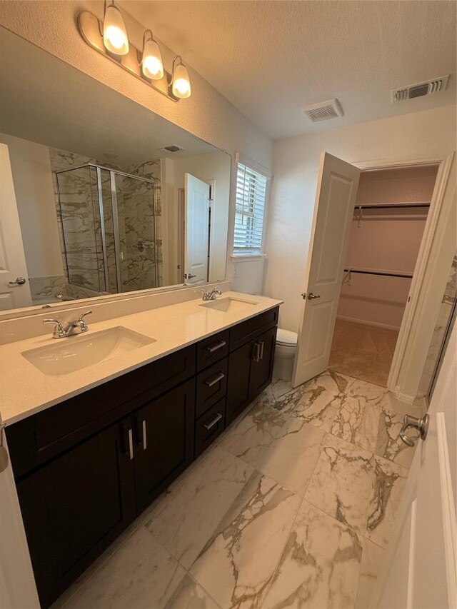 577 Backstays Loop, Kyle, TX 78640 - bathroom with a spacious closet, a stall shower, double vanity, a textured ceiling, and marble look tiles