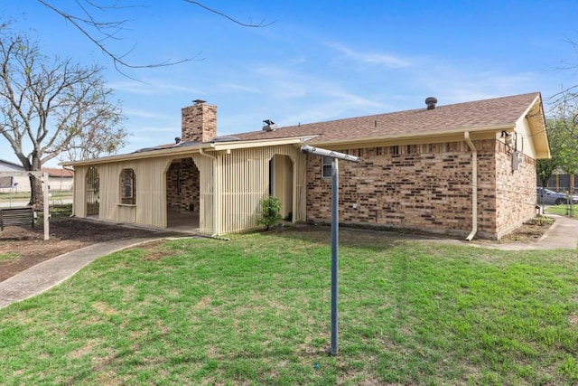 back of house with a chimney, brick siding, and a lawn