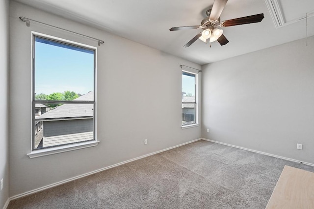 carpeted empty room featuring attic access, baseboards, and ceiling fan