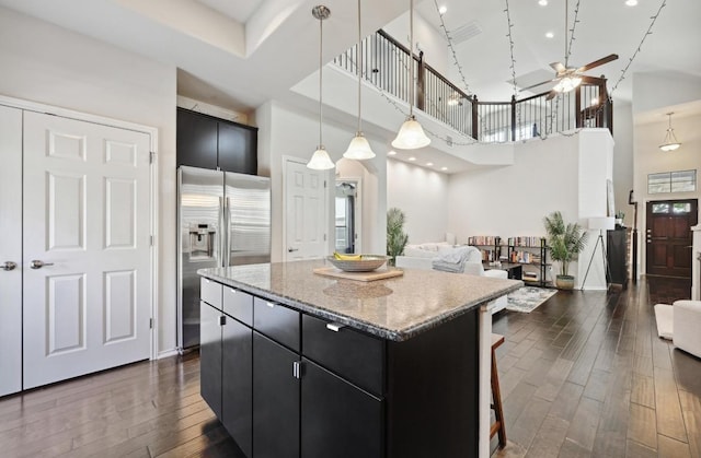 kitchen with dark wood finished floors, a towering ceiling, dark cabinetry, a center island, and stainless steel refrigerator with ice dispenser