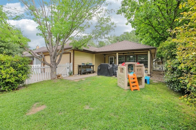 rear view of property with an attached garage, a lawn, and fence