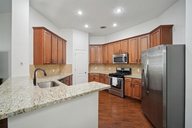 kitchen featuring light stone counters, a sink, a peninsula, appliances with stainless steel finishes, and dark wood-style floors