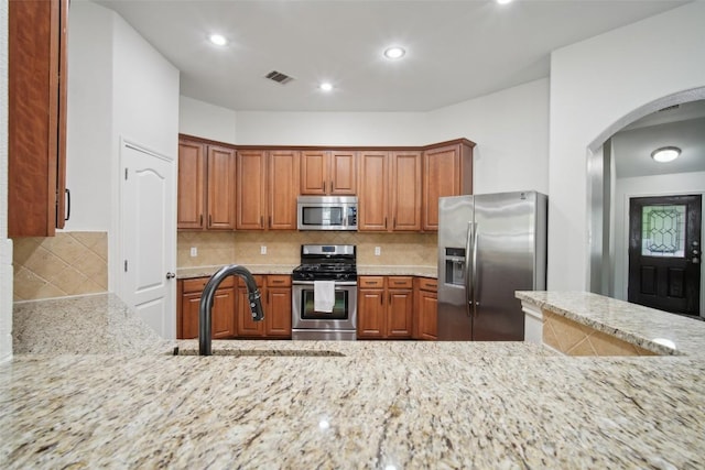 kitchen featuring visible vents, a sink, arched walkways, light stone countertops, and appliances with stainless steel finishes
