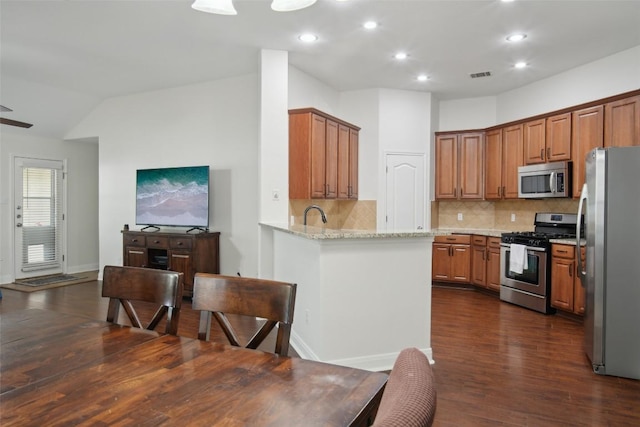 kitchen with brown cabinets, stainless steel appliances, dark wood finished floors, light stone countertops, and visible vents