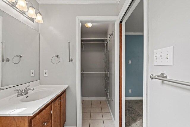 bathroom featuring a walk in closet, vanity, baseboards, ornamental molding, and tile patterned flooring