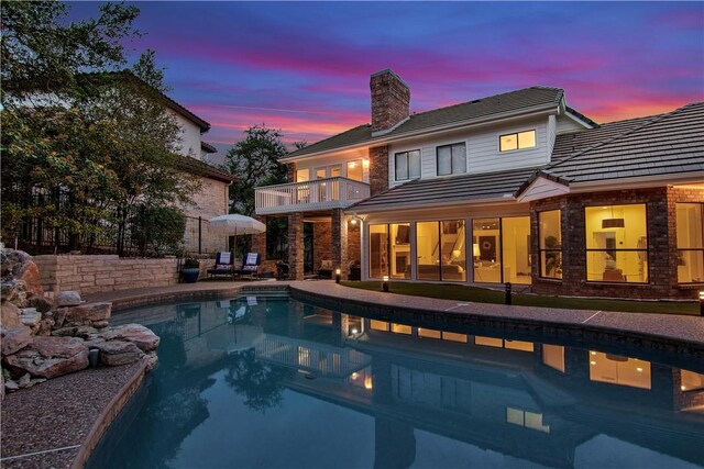 20 Hedgebrook Way, The Hills, TX 78738 - back of house at dusk with a balcony, a chimney, an outdoor pool, a tile roof, and a patio