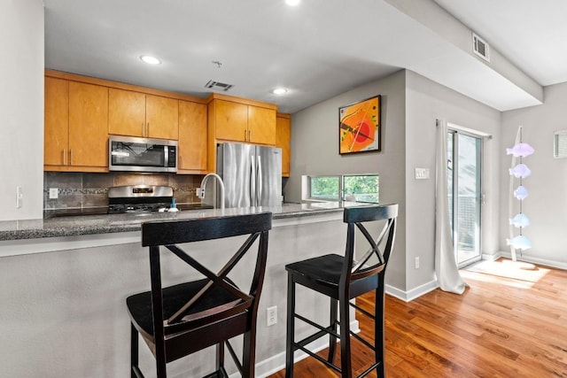 503 Swanee Dr Unit 11, Austin, TX 78752 - kitchen featuring appliances with stainless steel finishes, wood finished floors, decorative backsplash, recessed lighting, and a kitchen breakfast bar
