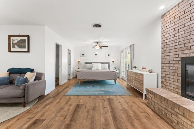 bedroom featuring a brick fireplace, wood finished floors, visible vents, and a ceiling fan