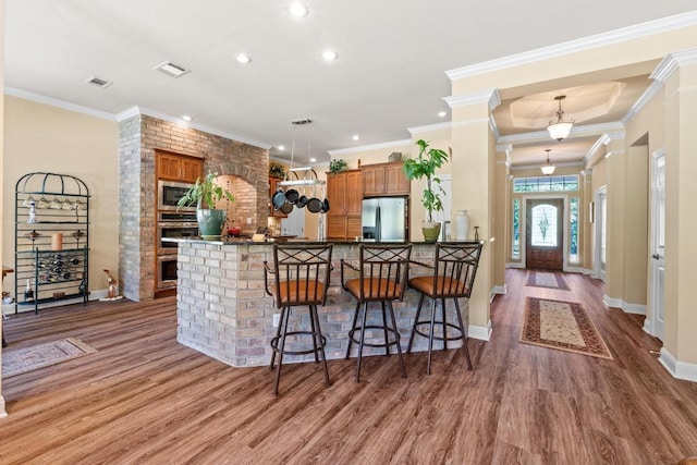 135 N Tumbleweed Trl, Austin, TX 78733 - kitchen with stainless steel appliances, brown cabinets, wood finished floors, a kitchen breakfast bar, and recessed lighting