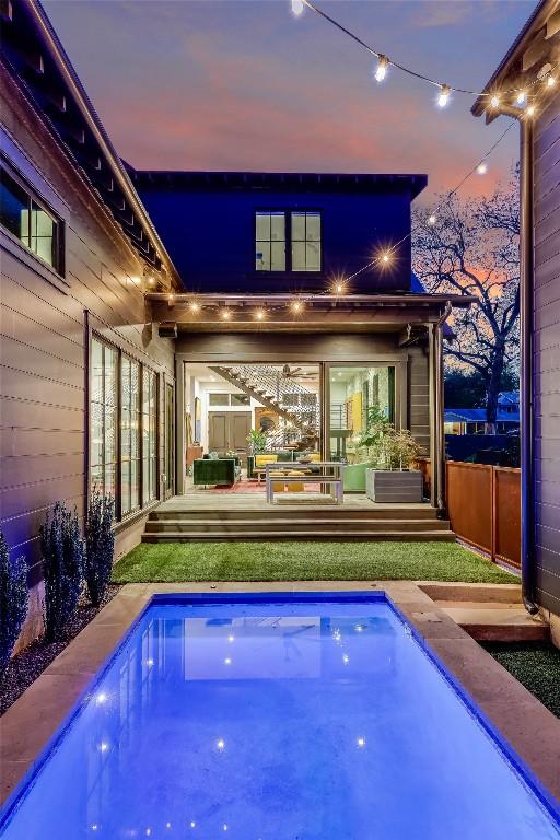 back of property at dusk with an outdoor pool and a deck