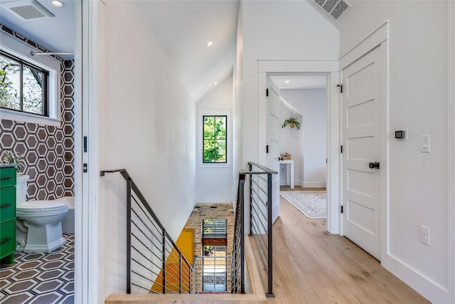 corridor with vaulted ceiling, wood finished floors, visible vents, and an upstairs landing