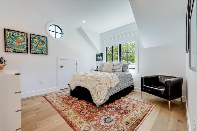 bedroom with vaulted ceiling, light wood finished floors, and baseboards