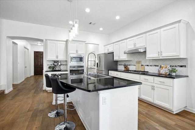 2216 Lookout Knoll Dr, Leander, TX 78641 - kitchen featuring stainless steel appliances, under cabinet range hood, arched walkways, decorative backsplash, and dark countertops