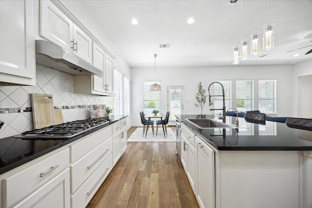 2216 Lookout Knoll Dr, Leander, TX 78641 - kitchen featuring under cabinet range hood, dark countertops, stainless steel gas stovetop, a sink, and backsplash